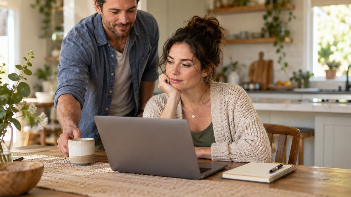 A couple reading together at a laptop on the kitchen table